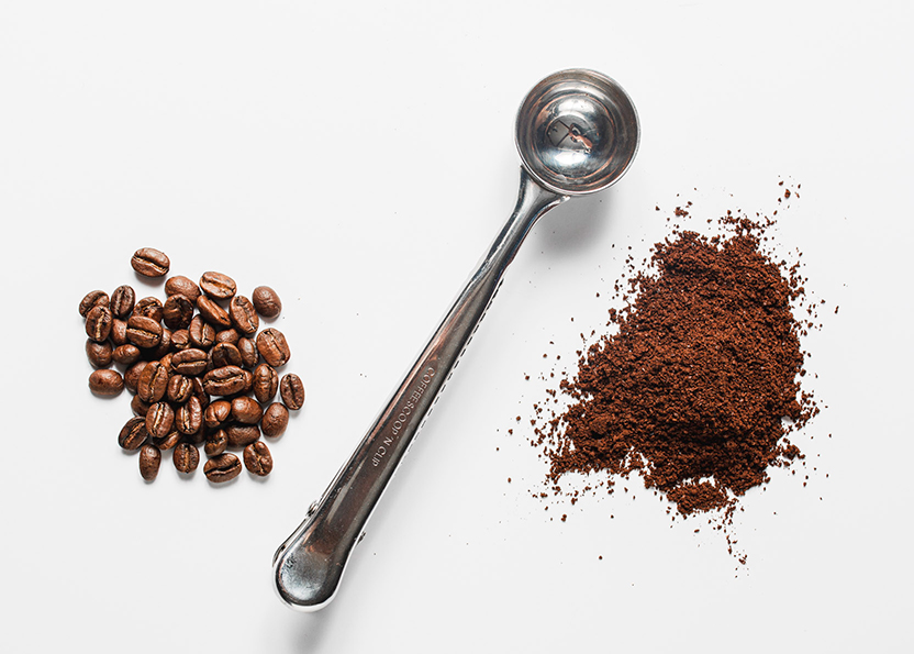Coffee beans, measuring spoon, coffee grounds. Image looks like spoon is dividing the beans from the grounds